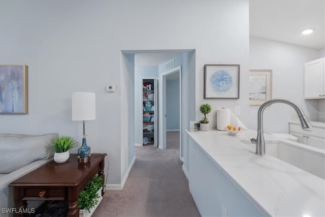 hall featuring lofted ceiling, sink, and light colored carpet