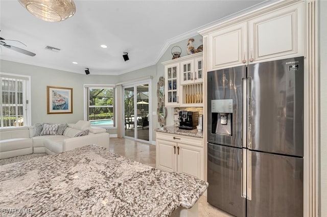 kitchen featuring ceiling fan, light stone counters, ornamental molding, and stainless steel refrigerator with ice dispenser