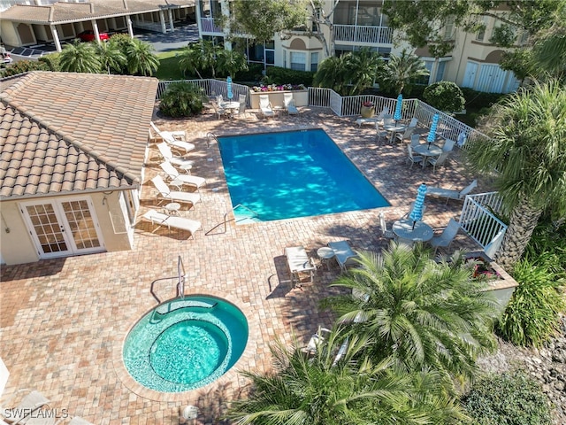 community pool with a hot tub, fence, and a patio