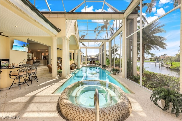 view of pool featuring a patio, an outdoor bar, glass enclosure, an in ground hot tub, and a water view