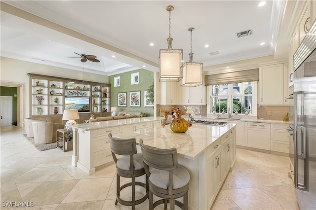 kitchen with light stone countertops, hanging light fixtures, a kitchen bar, a kitchen island, and ceiling fan