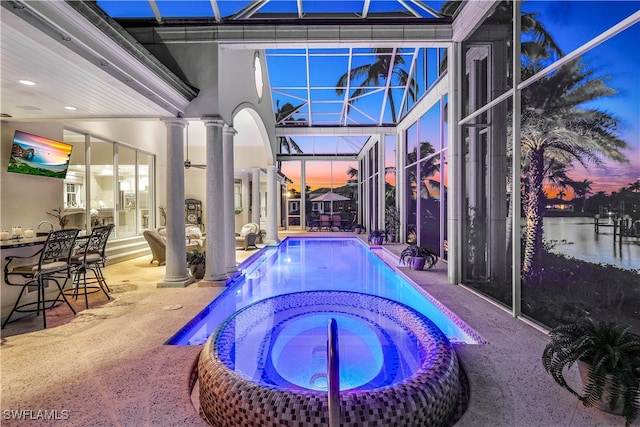 pool at dusk featuring a lanai, a patio, and an in ground hot tub