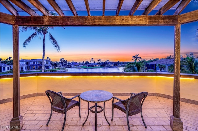 patio terrace at dusk featuring a pergola and a water view