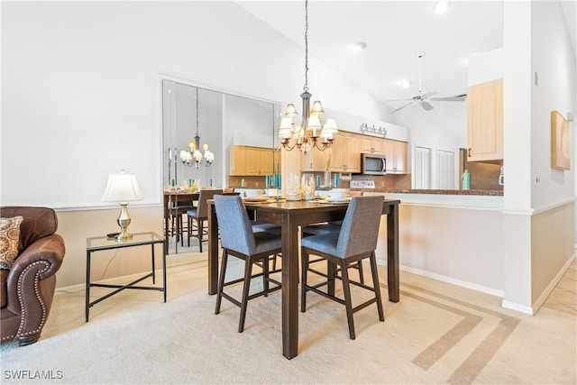 dining area with ceiling fan with notable chandelier, light colored carpet, and high vaulted ceiling