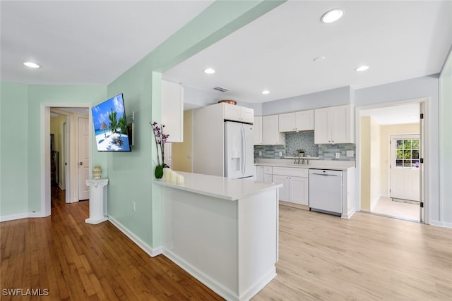 kitchen featuring white cabinetry, backsplash, kitchen peninsula, light hardwood / wood-style floors, and white appliances