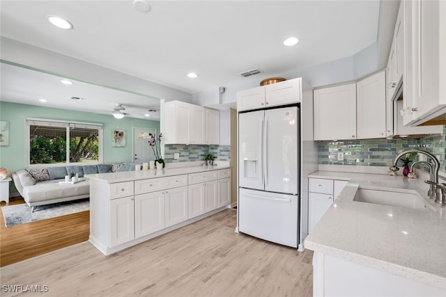 kitchen featuring light stone countertops, white fridge with ice dispenser, sink, white cabinets, and light wood-type flooring