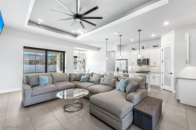 living room with ceiling fan, light tile patterned floors, sink, and a tray ceiling