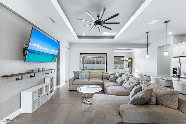 living room with ceiling fan with notable chandelier, dark tile patterned floors, and a tray ceiling