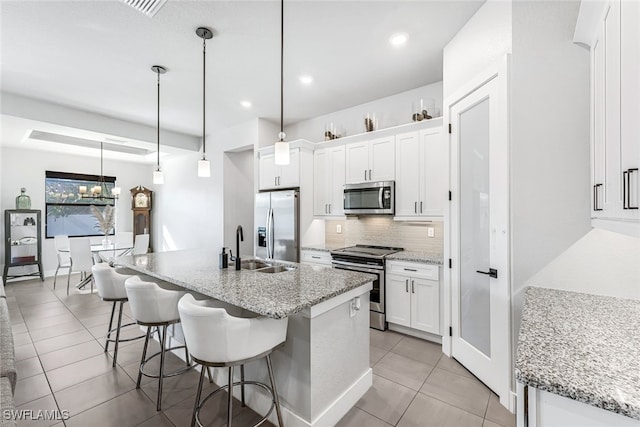 kitchen with a kitchen island with sink, light stone countertops, appliances with stainless steel finishes, decorative light fixtures, and white cabinetry