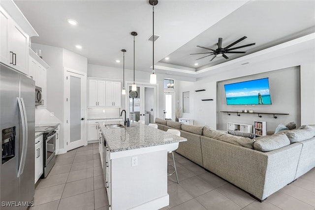 kitchen with white cabinetry, sink, stainless steel appliances, decorative light fixtures, and a center island with sink