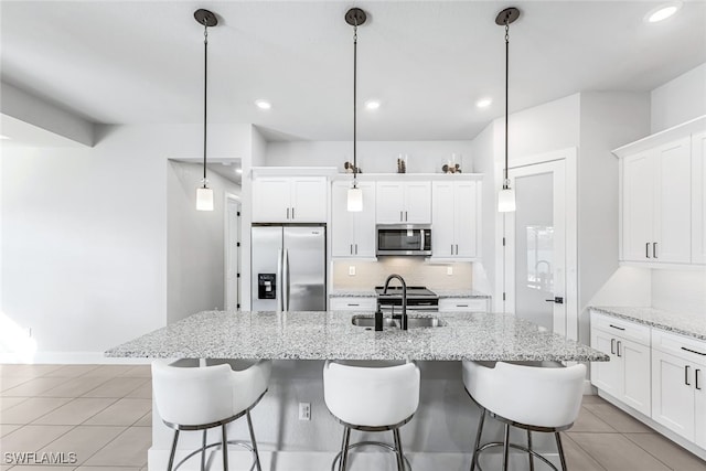 kitchen with appliances with stainless steel finishes, tasteful backsplash, sink, decorative light fixtures, and an island with sink