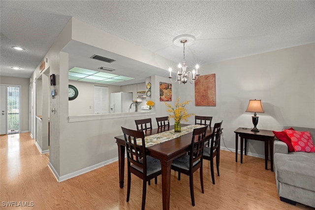 dining space with light hardwood / wood-style floors, a notable chandelier, a textured ceiling, and sink