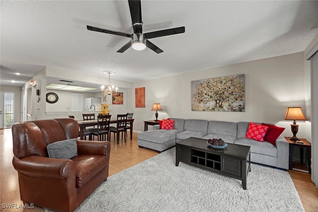 living room featuring light wood-type flooring, ceiling fan with notable chandelier, and a textured ceiling