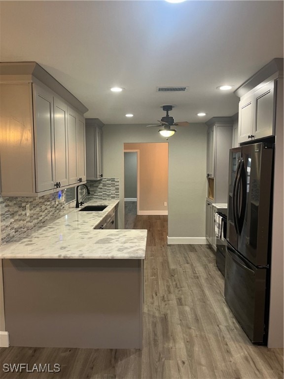 kitchen with kitchen peninsula, gray cabinetry, sink, wood-type flooring, and fridge