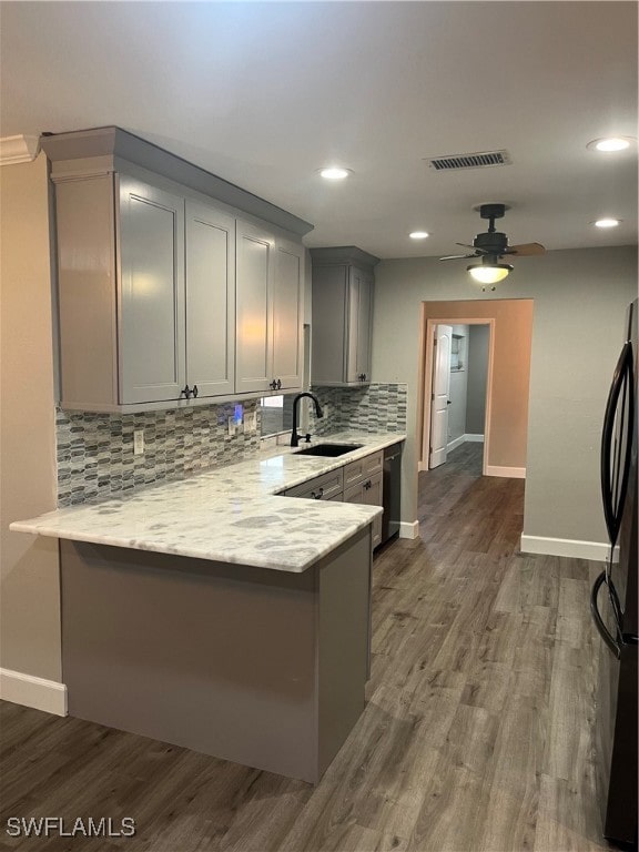 kitchen with kitchen peninsula, stainless steel fridge, dark hardwood / wood-style flooring, sink, and gray cabinets