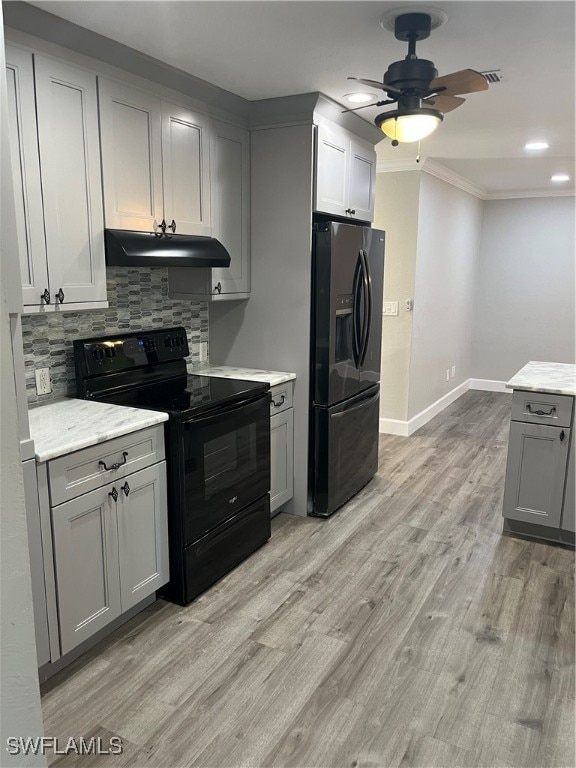 kitchen featuring gray cabinetry, light hardwood / wood-style flooring, decorative backsplash, black appliances, and ornamental molding