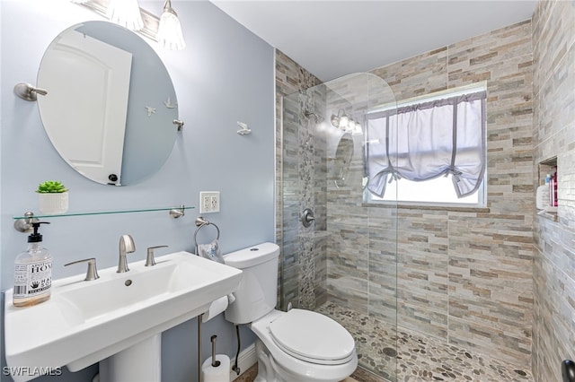 bathroom featuring tiled shower, toilet, and sink