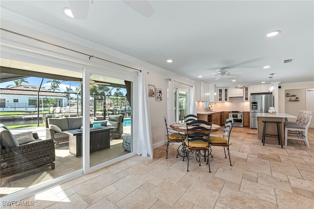 dining area with ceiling fan, plenty of natural light, crown molding, and sink