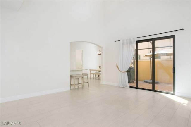 empty room featuring a towering ceiling, baseboards, and arched walkways