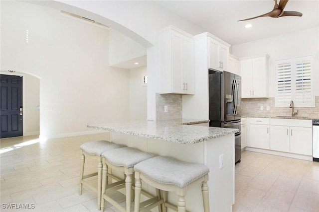 kitchen with light stone counters, a breakfast bar, a sink, white cabinets, and stainless steel refrigerator with ice dispenser