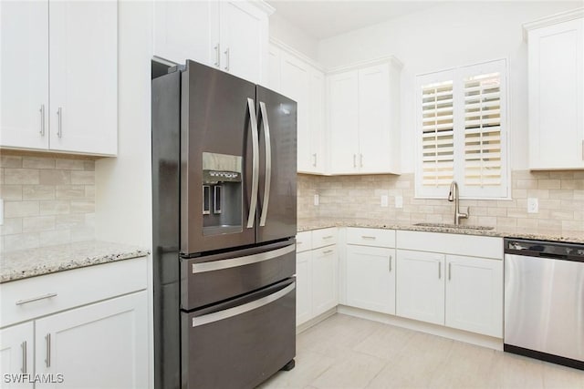 kitchen featuring white cabinets, light stone countertops, stainless steel appliances, and a sink