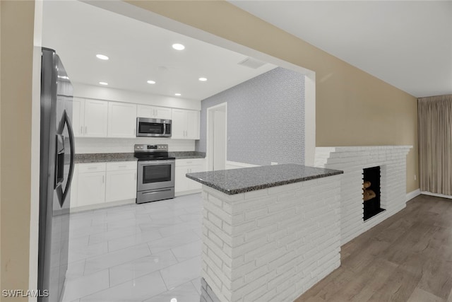 kitchen featuring white cabinets, kitchen peninsula, appliances with stainless steel finishes, and dark stone counters