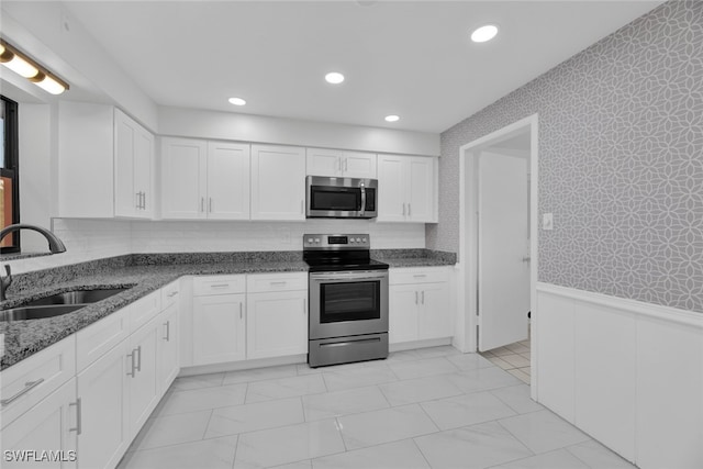 kitchen with white cabinetry, appliances with stainless steel finishes, sink, and dark stone countertops