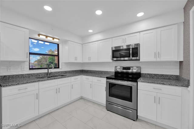 kitchen featuring stainless steel appliances, dark stone countertops, white cabinetry, and sink