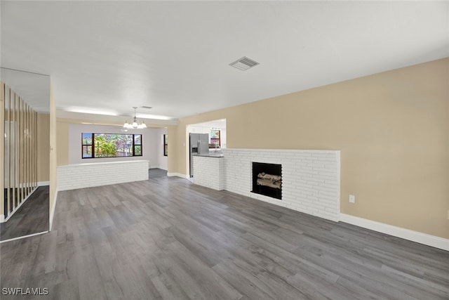 unfurnished living room featuring a brick fireplace, hardwood / wood-style flooring, and a chandelier