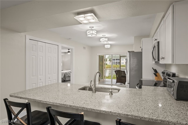 kitchen with a kitchen bar, white cabinets, sink, light stone countertops, and appliances with stainless steel finishes