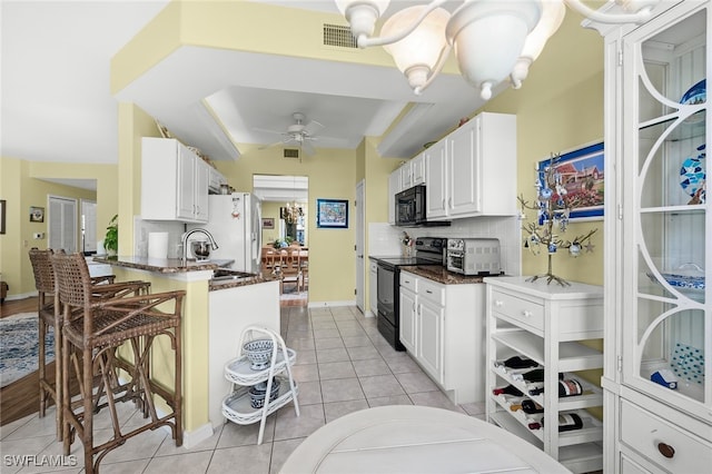 kitchen with light tile patterned floors, backsplash, a sink, black appliances, and ceiling fan with notable chandelier