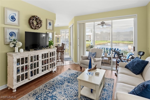 living room featuring ceiling fan with notable chandelier, wood finished floors, and baseboards