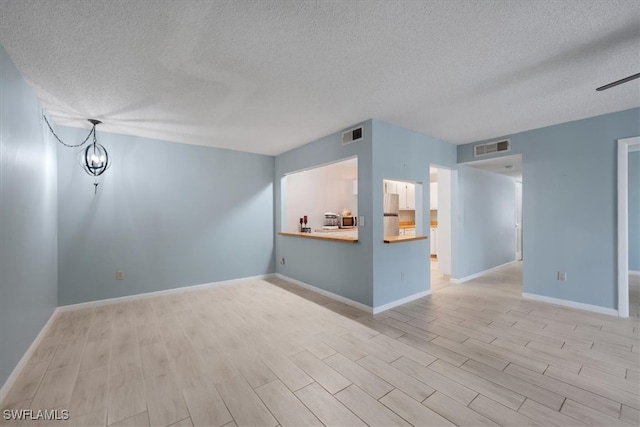 unfurnished room featuring light hardwood / wood-style floors, a textured ceiling, and a chandelier