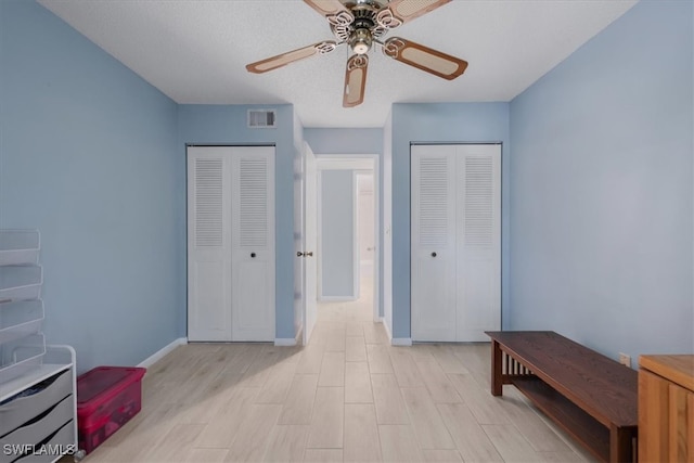 interior space featuring a textured ceiling, multiple closets, ceiling fan, and light wood-type flooring