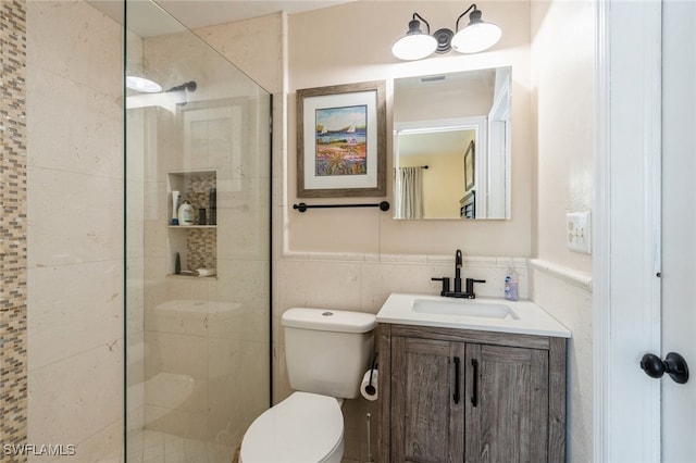 bathroom featuring tile walls, tiled shower, vanity, and toilet