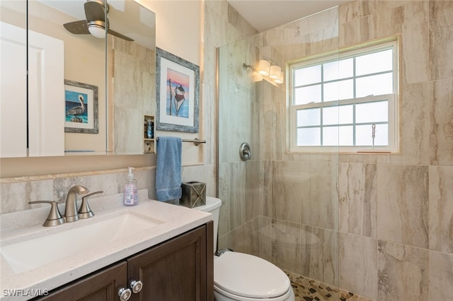 bathroom with ceiling fan, vanity, toilet, and tiled shower