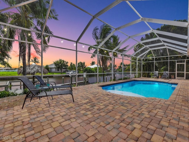 pool at dusk featuring a water view, a lanai, a boat dock, and a patio area