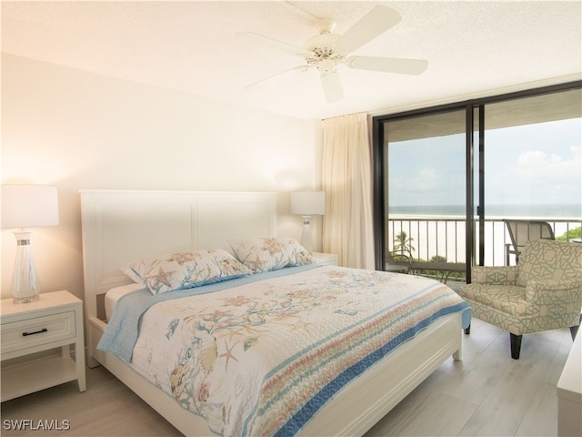 bedroom with a water view, ceiling fan, a wall of windows, light wood-type flooring, and access to outside