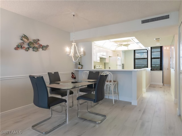 dining space featuring ceiling fan with notable chandelier, a textured ceiling, and light hardwood / wood-style flooring