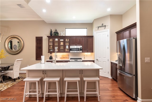 kitchen with a breakfast bar, dark brown cabinetry, stainless steel appliances, a center island with sink, and light hardwood / wood-style flooring