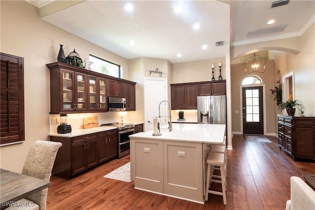 kitchen with hardwood / wood-style floors, a kitchen island with sink, crown molding, decorative backsplash, and appliances with stainless steel finishes