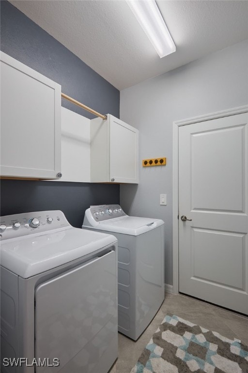 washroom with cabinets, a textured ceiling, and washing machine and dryer