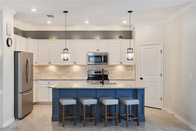 kitchen with ornamental molding, stainless steel appliances, white cabinets, hanging light fixtures, and an island with sink