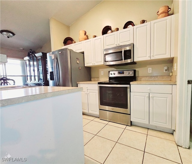 kitchen with white cabinetry, stainless steel appliances, light tile patterned flooring, and vaulted ceiling