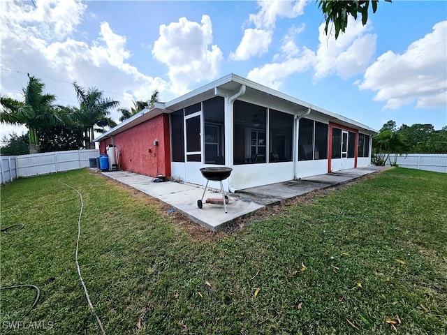 rear view of property featuring a lawn, a sunroom, and a patio