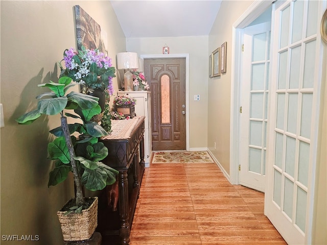 doorway to outside with light hardwood / wood-style flooring and vaulted ceiling