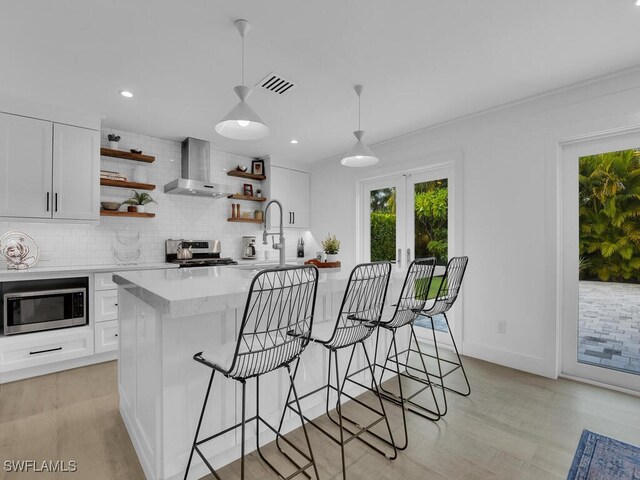 kitchen featuring white cabinets, pendant lighting, wall chimney range hood, and stainless steel appliances