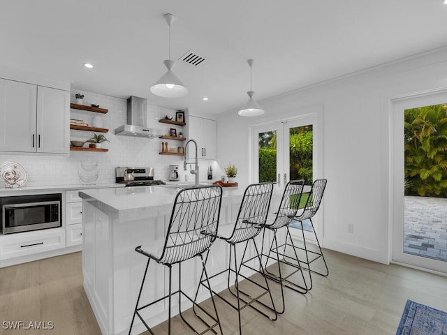 kitchen featuring appliances with stainless steel finishes, wall chimney exhaust hood, decorative light fixtures, and white cabinets