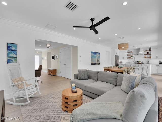 living room with ornamental molding, ceiling fan, and light wood-type flooring