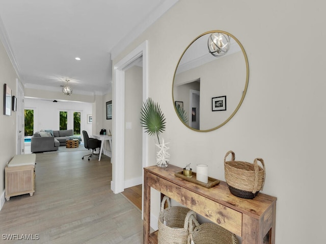 hallway with an inviting chandelier, crown molding, and light hardwood / wood-style floors